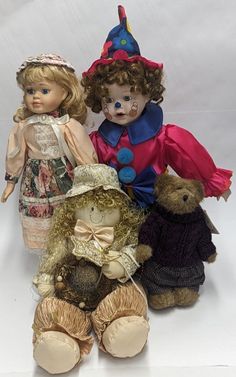 three dolls are sitting next to each other on a white surface, one is wearing a dress and the other has a hat