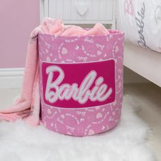 a pink bag with the word barbie on it sitting in front of a white bed