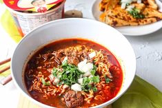 a bowl of soup with meat, noodles and vegetables in it next to two plates of food