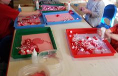 children are sitting at a table making valentine's day crafts with red and green trays