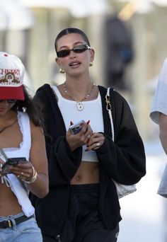 two women walking down the street with cell phones in their hands and one is looking at her phone