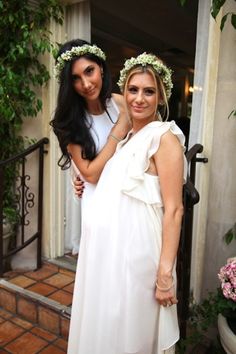 two beautiful women standing next to each other in front of a door with flowers on their head