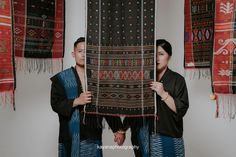 two people standing next to each other in front of rugs hanging on the wall