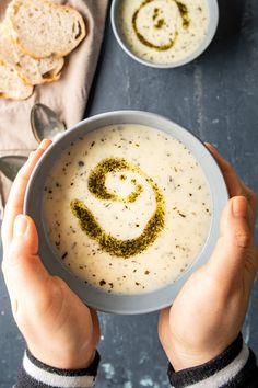 two hands holding a bowl of soup with a smiley face drawn on it