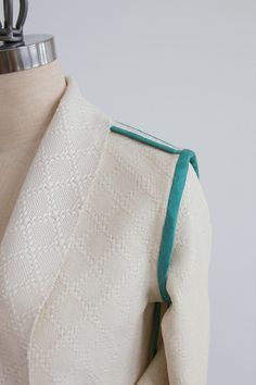 the back of a white jacket with green trims on it and a mannequin's torso