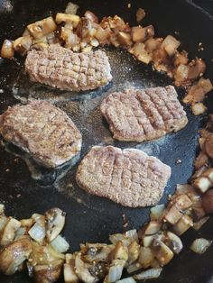 four hamburger patties cooking in a skillet with onions and mushrooms on the side