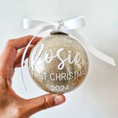 a hand holding a glass ornament that says rose first christmas