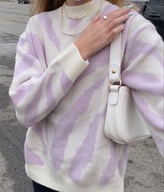 a woman wearing a purple and white striped sweater holding a white handbag in her right hand