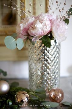 a vase filled with pink flowers sitting on top of a table next to christmas ornaments