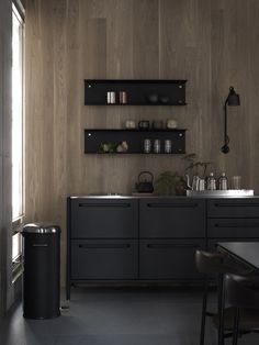 an empty kitchen with black cabinets and shelves on the wall, along with a dining room table