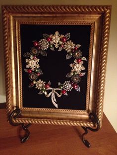 a gold frame with a wreath made out of beads and flowers on it sitting on a table