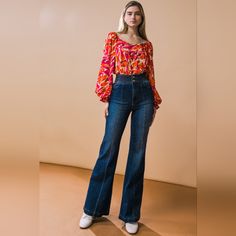 a woman standing in front of a wall wearing high rise jeans and a floral blouse