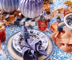 a table topped with plates and dishes covered in blue cloths next to pumpkins