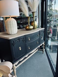 a black dresser with two gold vases on top and a white lamp next to it