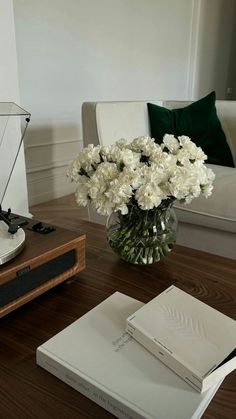 a vase with white flowers sitting on a table next to a book and record player