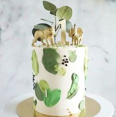 a white cake with green leaves and animals on top is sitting on a gold plate