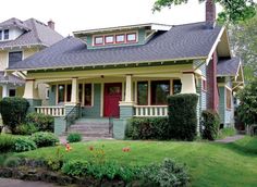 a green and yellow house with red door in the front yard, surrounded by greenery