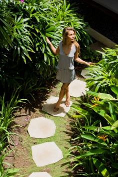 a woman walking down a path in the middle of lush green grass and plants with stepping stones on either side