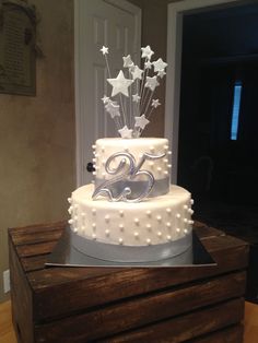 a three tiered cake with stars and balloons on top is sitting on a wooden box