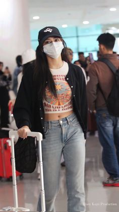 a woman wearing a face mask and holding a suitcase at an airport with other people in the background