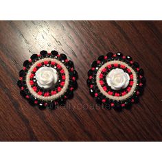 two red, white and black beaded earrings on a wooden table with a flower in the center