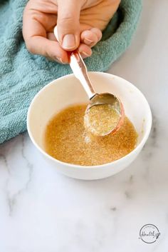 a person holding a spoon in a bowl filled with brown liquid on top of a blue towel