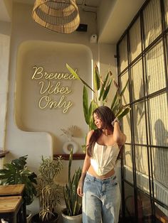 a woman standing in front of a window next to a plant and potted plants