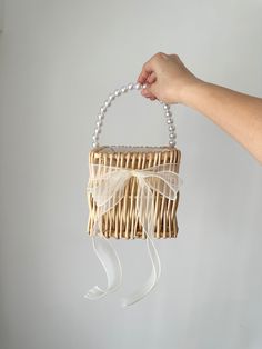 a hand holding a wicker purse with white ribbon and pearls hanging from it's side