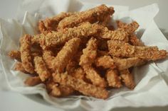 fried chicken sticks sitting in a basket on top of a white tableclothed cloth