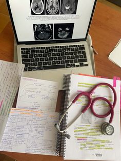 an open laptop computer sitting on top of a wooden desk next to a notebook and stethoscope