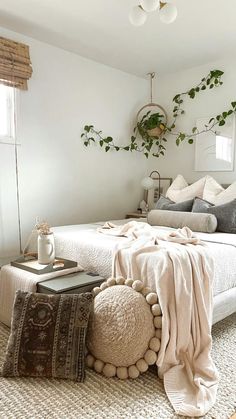 a bedroom with white walls and lots of pillows on the bed, plants hanging from the ceiling