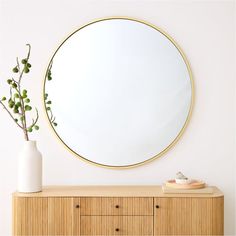 a round mirror sitting on top of a wooden dresser next to a vase filled with flowers