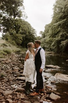 a bride and groom kissing in front of a stream on their wedding day at the riverbank