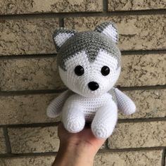 a hand holding a knitted stuffed animal in front of a brick wall