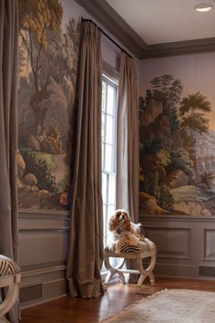 a dog is sitting on a chair in front of a wall with a landscape painted on it