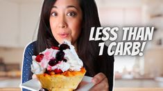 a woman is holding up a cupcake with whipped cream and berries on top, while looking at the camera