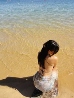 a woman sitting on top of a sandy beach next to the ocean