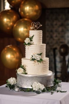 a three tiered wedding cake sitting on top of a table next to gold balloons