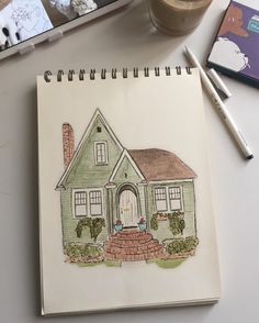 a drawing of a house on a notebook next to a cup of coffee and markers