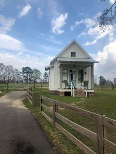 a small white house sitting on top of a lush green field next to a wooden fence