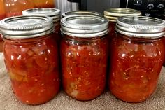 four jars filled with red peppers sitting on top of a counter next to an oven