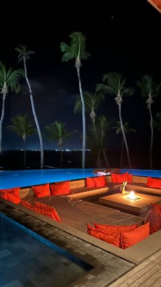 an outdoor seating area with fire pit and palm trees in the background at night time