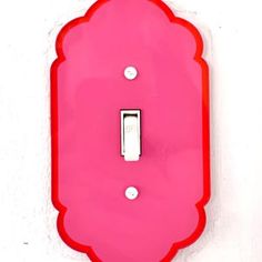 a pink light switch cover on a white wall with a red scalloped design