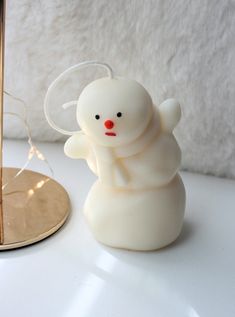 a white candle with a red nose and an angel on it sitting next to a mirror