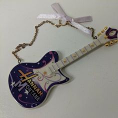 a guitar shaped keychain hanging from a chain on a white surface with a ribbon around it