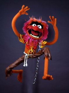 an orange and pink puppet is hanging from a chain with its arms in the air