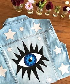 a denim jacket with an eye painted on the back and stars in the front, sitting on a wooden table