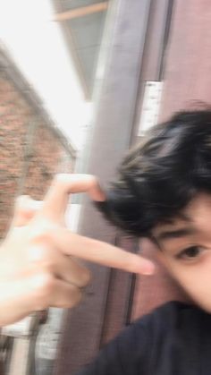 a young boy making a hand sign with his fingers while standing in front of a brick building