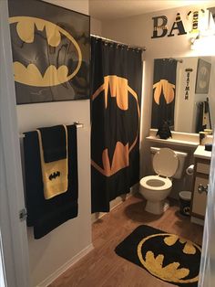 a bathroom decorated in black and yellow with batman decorations on the shower curtain, toilet seat cover and rug