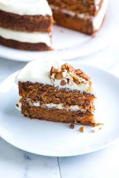 a slice of carrot cake with white frosting and pecans on the top is sitting on a plate